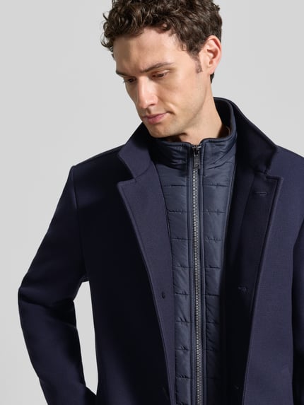 Männermodel trägt Regular Fit Mantel mit Knopf- und Reißverschluss von ROY ROBSON, kolor granatowy, płaszcz z stójką, Brustasza, wpuszczane kieszenie, Długość tyłu w rozmiarze 50: 91 cm, Szerokość ramion w rozmiarze 50: 47 cm, Szerokość klatki piersiowej w rozmiarze 50: 55 cm, Długość rękawów w rozmiarze 50: 69 cm, tekstura gładka, Nahaufnahme Oberkörper