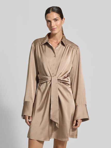Frauenmodel trägt knielanges Hemdblusenkleid mit Knotendetail Modell 'Biria' von Neo Noir in Satin, gerade Form, beige, Nahaufnahme Oberkörper.