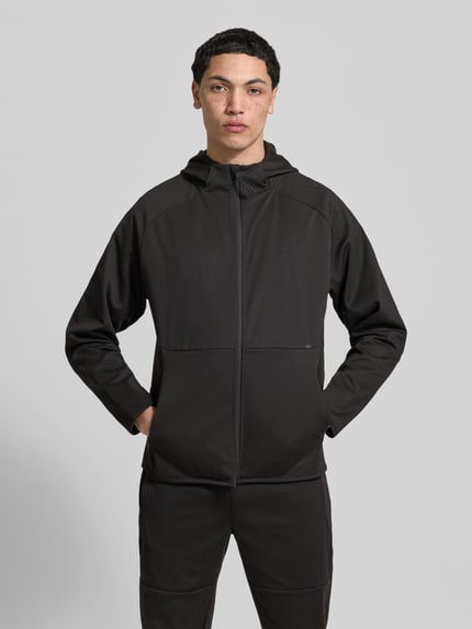 Männermodel trägt Regular Fit Sweatjacke mit Kapuze Modell 'Base' von Jack & Jones in Schwarz, sichtbare Reißverschlusstaschen, Ganzkörperansicht von vorne, elastischer Material-Mix mit Baumwoll-Anteil.