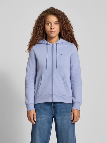 Kobiece model prezentuje Regular Fit Sweatjacke aus Baumwoll-Mix od Tommy Jeans, jasnofioletowa, jednolita, z kapturem, bawełniany dres; całkowity widok z przodu.