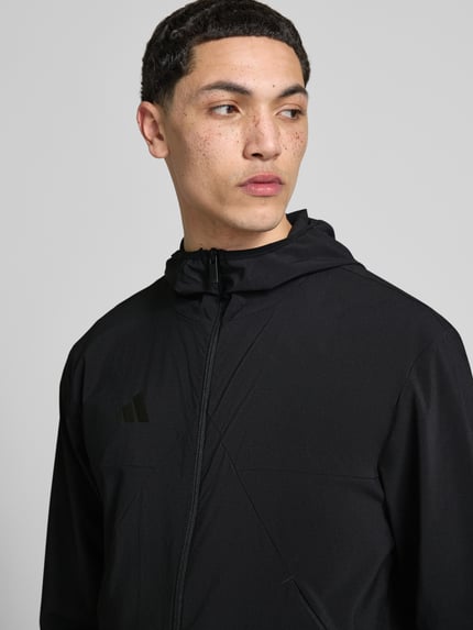 Mężczyznamodel nosi Slim Fit Funktionsjacke aus schnelltrocknendem Material von adidas Sportswear, efekt: jednolity kolor, krój slim fit, kształt kołnierza: kaptur, zapięcie: zamek błyskawiczny, aplikacja: nadruk z logo, rękawy: długi rękaw, funkcja: szybkoschnący, z regulacją wilgoci, boczna kieszeń zapinana na zamek błyskawiczny, materiał gładki, czarny kolor, nahaufnahme górnej części ciała