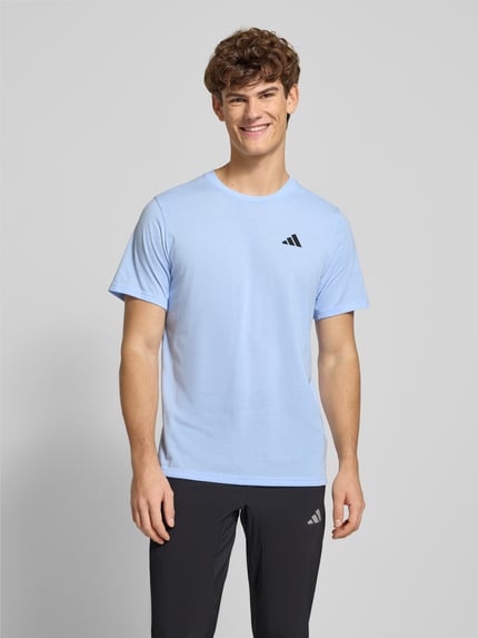 Männermodel trägt T-Shirt mit Label-Print von adidas Training, hellblau, Baumwoll-Mix, Regular-Fit, gerippter Rundhalsausschnitt, Ganzkörperansicht von vorne. Rückenlänge bei Größe M: 74 cm.