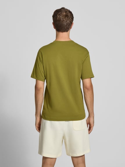 Männermodel trägt olivgrünes T-Shirt mit Label-Stitching Modell 'ESSENTIALS' von New Balance aus reiner Baumwolle, gerader Schnitt, Rundhalsausschnitt, Rückenlänge 68 cm bei Größe M, Ganzkörperansicht Rückansicht.