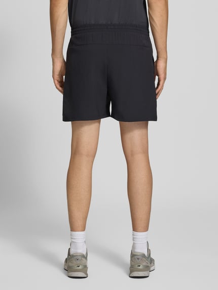 Männermodel trägt Shorts mit elastischem Bund und Logo von New Balance in Schwarz, glatte Textur, Herren Shorts, Ganzkörperansicht Rückansicht.