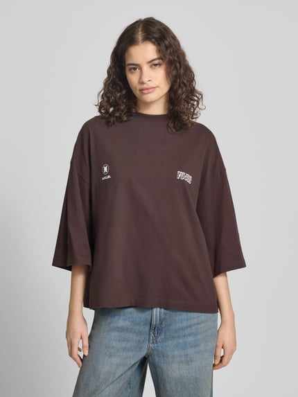 Frauenmodel trägt Oversized T-Shirt mit Rundhalsausschnitt von Karo Kauer, reine Baumwolle, Label-Print, dunkelbraun, Nahaufnahme Oberkörper.
