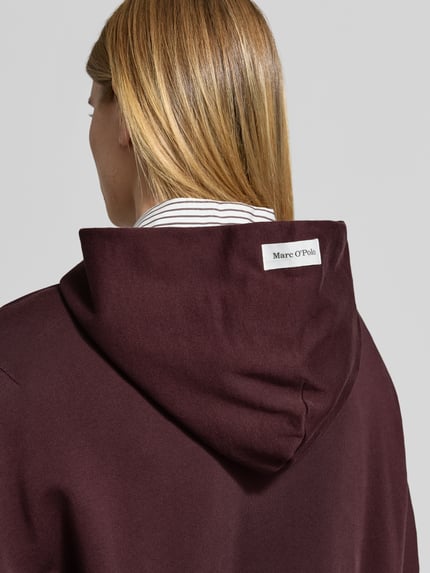 Frauenmodel trägt Sweatshirt mit Kapuze und Label-Detail von MARC O'POLO, bordeaux, Jersey, unifarben, Rückansicht Nahaufnahme Oberkörper.