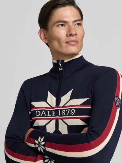 Männermodel trägt Wollpullover mit Label-Print Modell 'Nale' von Dale of Norway in Dunkelblau mit roten und weißen Streifen, Nahaufnahme Oberkörper, gerader Schnitt, Troyer-Kragen, reine Wolle, KI-modifiziertes Bild.