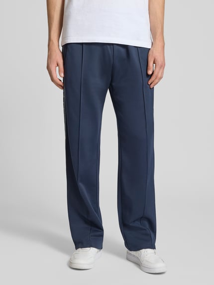 Mannenmodel draagt Trainingshose met Biese, opgestikt band en logo-borduursel van REVIEW, regular fit, blauwe stof, elastische tailleband, detailopname vooraan, binnenbeenlengte maat M: 43 cm.