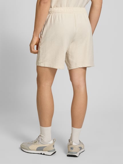 Männermodel trägt Shorts mit Logo-Stitching von PUMA PERFORMANCE in Beige mit Strukturmuster, elastischem Bund, geradem Schnitt, Ganzkörperansicht Rückansicht.