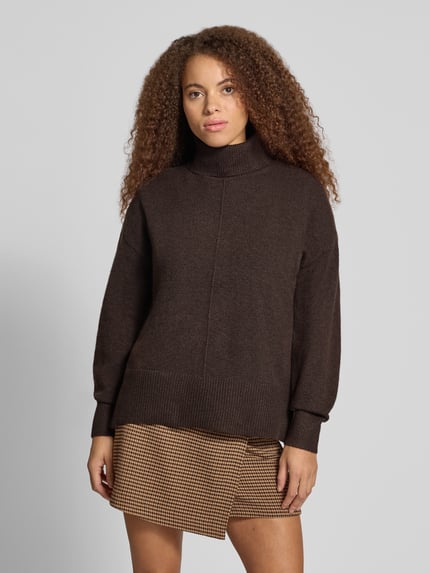 Frauenmodel trägt Rollkragenpullover mit Teilungsnaht von PIECES in brauner Melange-Strickoptik mit Strukturmuster, Ganzkörperansicht von vorne.