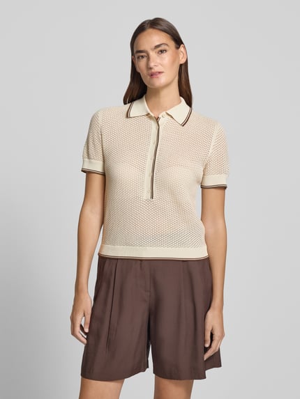 Kobiece modelka nosi Strickshirt mit Polokragen und Knopfleiste Modell 'MEROPE' od DRYKORN, czysta bawełna, krój regular fit, długość tyłu 50 cm, długość rękawa 20 cm, jasny beż z brązowymi detalami, faktura dzianiny, przód, zdjęcie górnej części ciała.