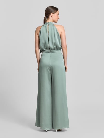 Kobiece model prezentuje Jumpsuit mit Schluppe und rückseitigem Knopfverschluss od Swing, satynowy materiał, krój slim fit, kolor miętowy, pasek w talii, długość całkowita 152 cm, długość nogawki wewnętrznej 82 cm, szerokość w rozmiarze 36: 66 cm, długość pleców 37 cm, zapięcie na guziki, haczyk i zamek z tyłu, widok całej sylwetki z tyłu.