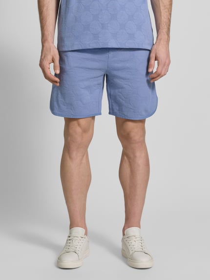 Mannelijk model draagt Regular Fit Shorts uit katoenmix model 'JT_Member Short' van BOSS Green, grafisch gestructureerd, uni, blauwe kleur, sweatmateriaal, elastische tailleband, steekzakken, detailopname voorkant.