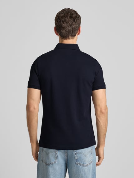 Männermodel trägt Slim Fit Poloshirt mit Stretch-Anteil von Tommy Hilfiger in Dunkelblau, Baumwoll-Elasthan-Mix, Ganzkörperansicht Rückansicht.