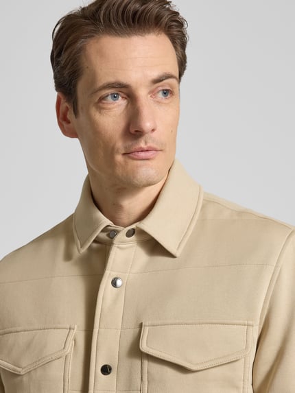 Männermodel trägt Regular Fit Sweatjacke aus Baumwoll-Mix von Tommy Hilfiger in Beige, unifarben, mit Druckknopfleiste, Nahaufnahme Oberkörper.