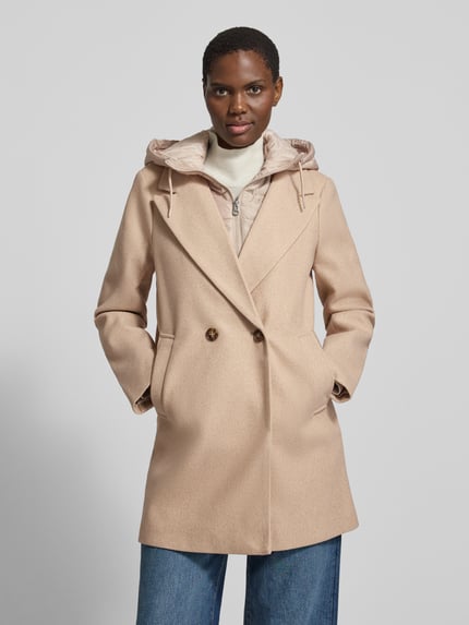 Frauenmodel trägt Mantel mit abnehmbarer Kapuze Modell 'VMGRACE' von VERO MODA in Beige, einfarbig, strukturierte Webware, Zierknöpfe, seitliche Taschen, Reverskragen, Longline, Regular Fit, Ganzkörperansicht von vorne.