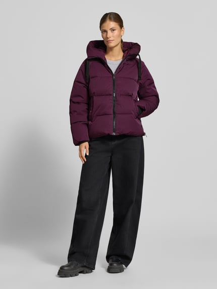 Frauenmodel trägt Regular Fit Steppjacke aus Material-Mix Modell 'Pavinaria' von MSCH Copenhagen in dunklem Lila, glatte Struktur, Ganzkörperansicht von vorne, Damen Steppjacke mit Kapuze und Reißverschluss, Eingrifftaschen, Rückenlänge 60 cm, Schulterbreite 48 cm, Brustweite 52 cm, Ärmellänge 59 cm.