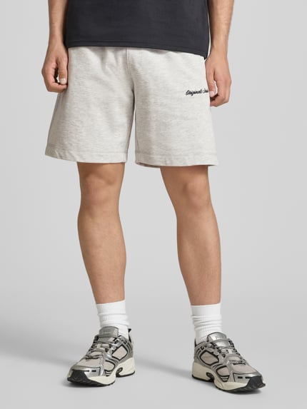Männermodel trägt Shorts mit Label-Stitching Modell 'KARL' von Jack & Jones aus Baumwoll-Mix, Relaxed-Fit, helle Farbe, seitliche Eingrifftaschen, elastischer Bund mit Kordelzug, Ganzkörperansicht von vorne.