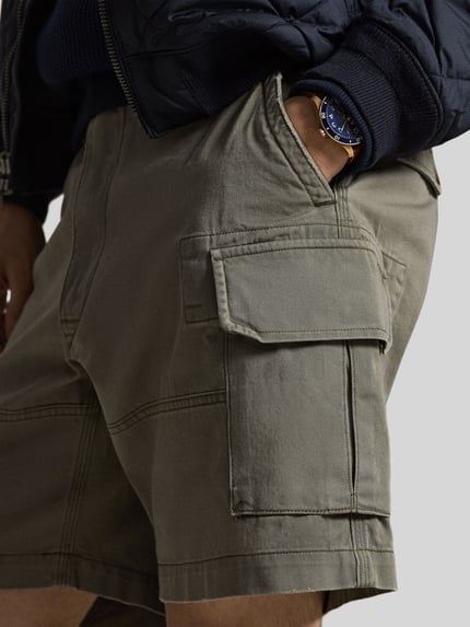 Männermodel trägt Relaxed Fit Cargoshorts aus reiner bawełna von Polo Ralph Lauren, efekt: jednolity kolor, wyhaftowane logo, szlufki na pasek, zapięcie na guzik i zamek błyskawiczny, wpuszczane kieszenie boczne, kieszenie z tyłu z guzikiem, kieszenie cargo, tkana faktura, Nahaufnahme okolicy bioder.