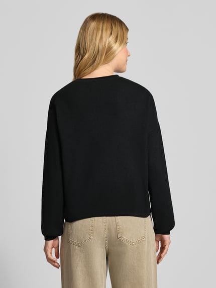 Frauenmodel trägt Strickpullover aus Viskose-Mix mit Rundhalsausschnitt von MORE & MORE, schwarzer Regular Fit, Label-Detail, Tunnelzug, Rückansicht, Rückenlänge 53 cm, Ärmellänge 48 cm.