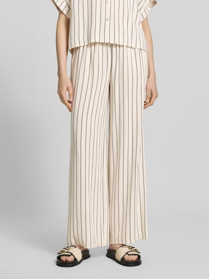 Frauenmodel trägt Loose Fit Weite HOSE aus Viskose-Leinen-Mix Modell 'VIVA-GULIA' von Selected Femme, Optik:Allover-Muster, Gestreift, High-Waist, Bundabschluss: elastisch mit Tunnelzug, Eingrifftaschen, Naturfarben mit braunen Streifen, strukturierte Textur, Ganzkörperansicht von vorne.