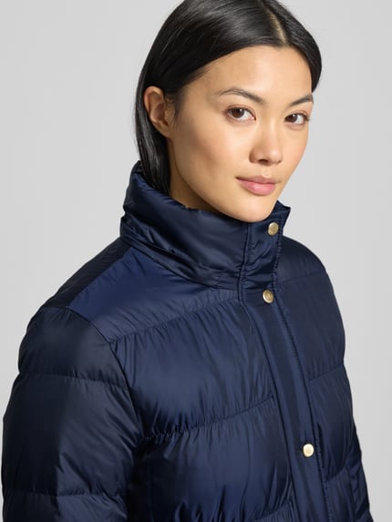 Vrouwenmodel draagt Steppmantel met Kapuze und Reißverschlusstaschen van Lauren Ralph Lauren in donkerblauw, detailopname bovenlichaam, regular fit, kunstbontkap, rits- en knoopsluiting, zakken met rits, maat S ruglengte 104 cm, schouderbreedte 38 cm, borstwijdte 47 cm, mouwlengte 60 cm.