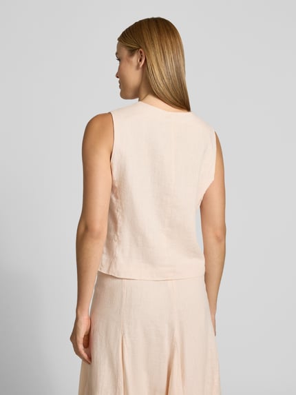 Frauenmodel trägt Leinenweste mit V-Ausschnitt und Paspeltaschen von Emily Van den Bergh aus reinem Leinen in Hellbeige, Rückenansicht.