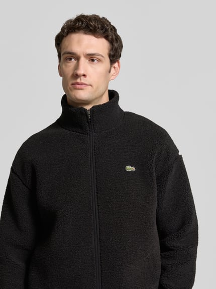 Männermodel trägt Bomberjacke mit Logo-Detail von LACOSTE in Schwarz, Stehkragen, langarm, elastische Abschlüsse, Nahaufnahme Oberkörper.