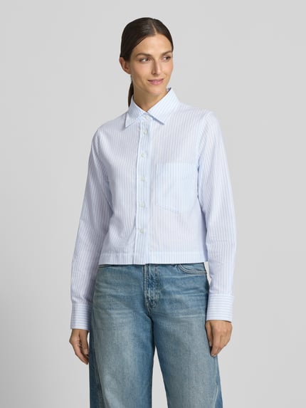 Modelka kobieca ma na sobie Hemdbluse mit Knopfleiste und Sportmanschetten od Closed, bawełna, krój regular fit, jasnoniebieskie paski, widok całej sylwetki od przodu.