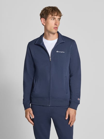 Mężczyzna nosi 'Sweatanzug mit Label-Details' od Champion w kolorze granatowym, Mieszanka bawełny, prosty krój, stójka, zamek błyskawiczny, detale z logo, wpuszczane kieszenie boczne, elastyczny pas, Szerokość w rozmiarze M: 76 cm, Długość tyłu w rozmiarze M: 70 cm, Szerokość ramion w rozmiarze M: 51 cm, Długość rękawów w rozmiarze M: 69 cm, Długość wewnętrzna nogawki w rozmiarze M: 76 cm, Ganzkörperansicht z przodu