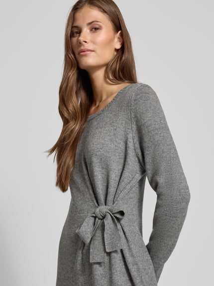 Frauenmodel trägt Relaxed Fit Kleid aus Woll-Mix in Strick-Optik Modell 'Protect' von Comma, grauer Farbton, Zierschleife, Nahaufnahme Oberkörper, Damen Kleid, Modal-Anteil, langärmelig, Rundhalsausschnitt, Rückenlänge 125 cm, Brustweite 46 cm, Ärmellänge 61 cm.