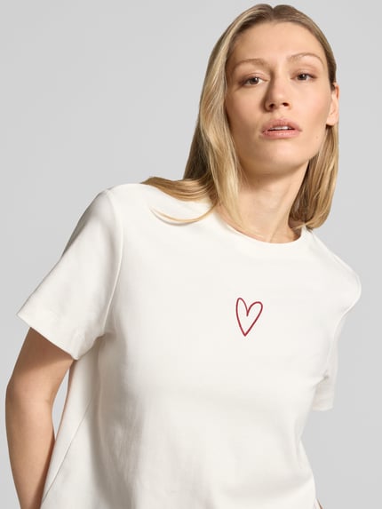 Frauenmodel trägt Oversized T-Shirt aus reiner Baumwolle Modell 'SARA METTE' von Vero Moda, unifarben, Herz-Stitching, Nahaufnahme Oberkörper.