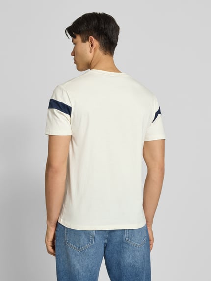 Männermodel trägt Regular Fit T-Shirt mit Logo-Detail Modell 'Caserio' von Ellesse, weiß mit dunkelblauen Akzenten, Jeans, Ganzkörperansicht Rückansicht.