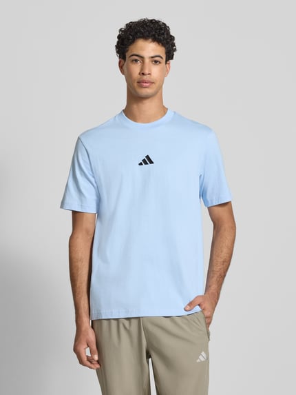 Męski model nosi T-Shirt mit Label-Detail od adidas Sportswear, jasnoniebieski, czarna aplikacja, krój regular fit, bawełna, widok z przodu, zdjęcie całej sylwetki.