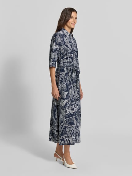 Frauenmodel trägt Hemdblusenkleid aus Viskose-Mix mit Bindegürtel von Christian Berg Woman, A-Linie, Allover-Muster, Seitansicht, Ganzkörperansicht von vorne.