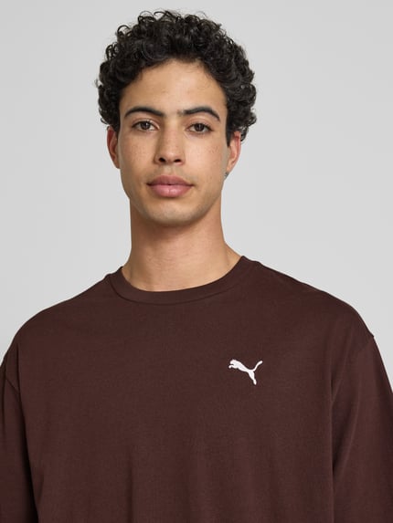 Männermodel trägt T-Shirt mit Rundhalsausschnitt von PUMA PERFORMANCE in Braun, Reine Baumwolle, Relaxed-Fit, mit Logo, Nahaufnahme Oberkörper.