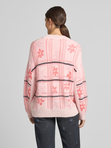 Frauenmodel trägt Oversized Cardigan mit Alpaka-Mohair-Anteil von Marc Cain in Rosa mit floralem Muster, Rückenansicht, Material-Mix.