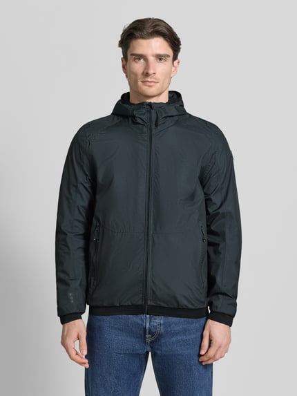 Männermodel trägt Jacke mit Kapuze Modell 'KOS' von Killtec in Schwarz, Gerader-Schnitt, Label-Patch, Reißverschlusstaschen, Ganzkörperansicht von vorne.