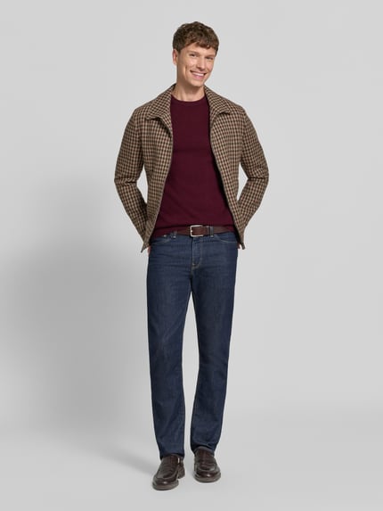 Männermodel trägt Kaschmirpullover mit gerippten Abschlüssen von Christian Berg Men in Dunkelrot, kombiniert mit brauner Jacke und Jeans, gerader Schnitt, Rundhalsausschnitt, reine Kaschmirqualität, Ganzkörperansicht von vorne.