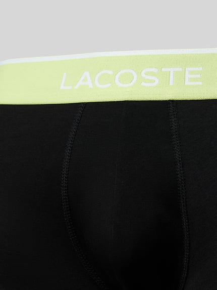 Männermodel trägt Trunks aus Baumwoll-Mix im 3er-Pack von Lacoste in Schwarz mit elastischem, gelbem Label-Bund, Nahaufnahme Oberkörper.