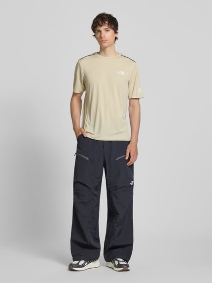 Männermodel trägt T-Shirt mit Logo und Rundhalsausschnitt von The North Face in Beige, Regular-Fit, glatte Textur, Ganzkörperansicht von vorne. Modell 'MOUNTAIN ATHLETICS', Rückenlänge bei Größe M: 66 cm, Herren T-Shirt.