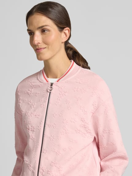 Kobieta modelka nosi Regular Fit Strickjacke aus Viskose-Mix von Marc Cain, mieszanka wiskozy z bawełną, stójka, zamek błyskawiczny dwustronny, paski w kontrastowym kolorze, różowy kolor, widoczna faktura, długość tyłu 59 cm, długość rękawów 58 cm, widok z przodu, zbliżenie na górną część ciała.