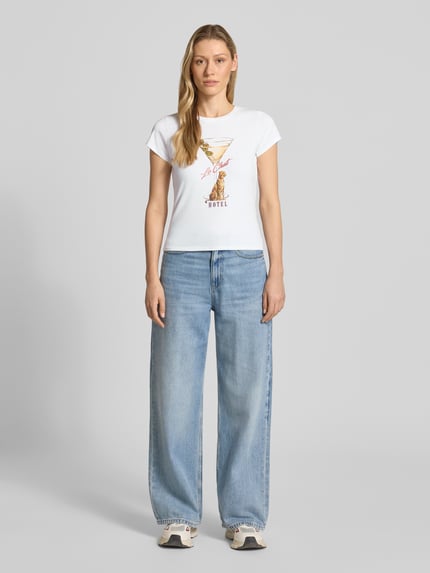 Frauenmodel trägt T-Shirt mit Label-Detail Modell 'LEOPARDTINI' von Guess in Weiß, körpernaher Schnitt, Baumwoll-Elasthan-Mix, Rundhalsausschnitt, Ganzkörperansicht von vorne.