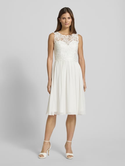 Vrouwenmodel draagt Brautkleid mit floraler Spitze van Mascara, wit, getailleerd, brede bandjes, hartvormige halslijn, semitransparant boven, ondoorzichtig onder, bloemmotief, haak- en ritssluiting, voorkant volledige lichaamsopname.