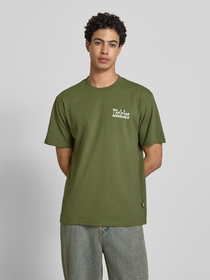 Männermodel trägt Herren T-Shirt mit Logo Modell 'VERNAL' von Dickies in Grün, Reine Baumwolle, Relaxed-Fit, Rundhalsausschnitt, Ganzkörperansicht von vorne.
