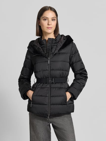 Frauenmodel trägt Jacke in Stepp-Optik von monari in Schwarz mit Kunstfell-Kapuze und taillierter Passform, Ganzkörperansicht von vorne.