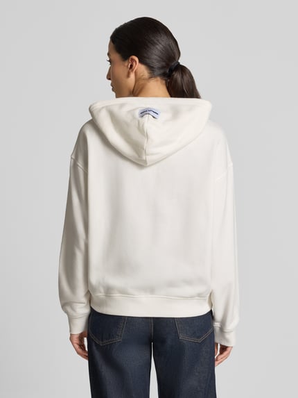 Frauenmodel trägt Oversized Sweatjacke aus Baumwoll-Mix Modell 'SOUL' von Smith and Soul in Creme mit Kapuze, elastischen Abschlüssen, Ganzkörperansicht Rückansicht.