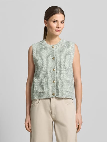 Kobiece model prezentuje Strickweste Melange Effekt mit Schmuckknopf od Christian Berg Woman, bawełniana mieszanka, krój regular fit, efekt melanżu, dekoracyjny guzik, ściągaczowe wykończenia, okrągły dekolt, zapięcie na guziki, kieszenie wpuszczane, długość tyłu w rozmiarze S: 51 cm, jasne pastelowe kolory, tekstura dzianiny, widok całej sylwetki z przodu.