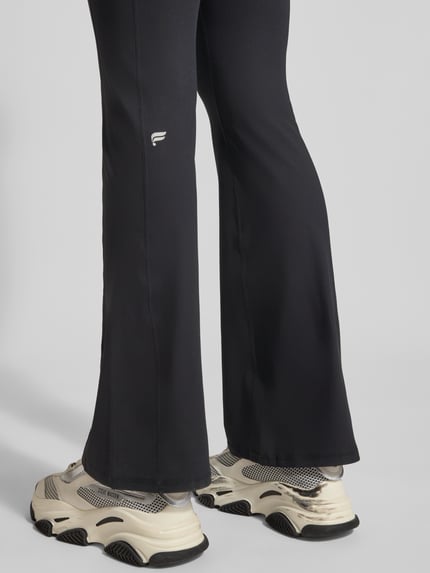 Frauenmodel trägt schwarze Flared Fit Leggins mit Logo-Print Modell 'OASIS' von Fabletics, elastischer Bund, Rückansicht, Detailaufnahme.