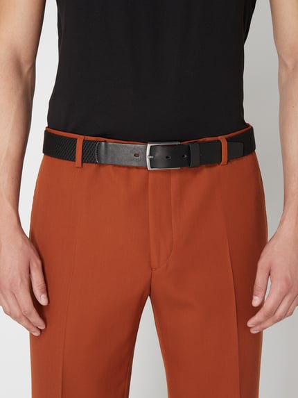 Männermodel trägt Gürtel mit Dornschließe von Lloyd Men's Belts in Schwarz, klassische Passform, kombiniert zu rostroter Hose, Nahaufnahme Oberkörper.